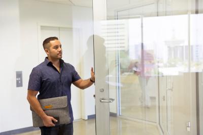 Man with laptop holding open a glass door in a office building